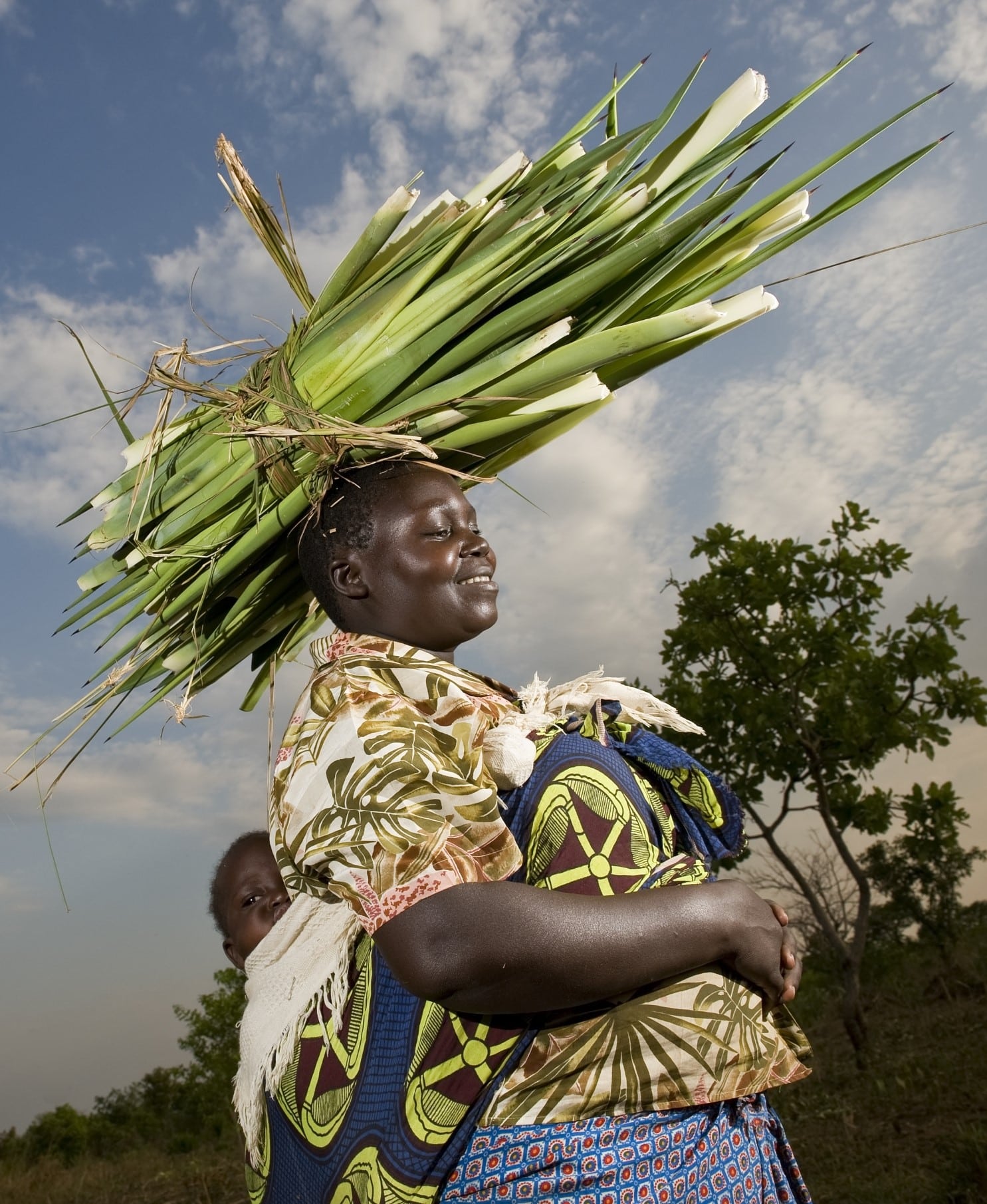 A female farmer in Uganda carrying her baby on her back and sisal on her head.