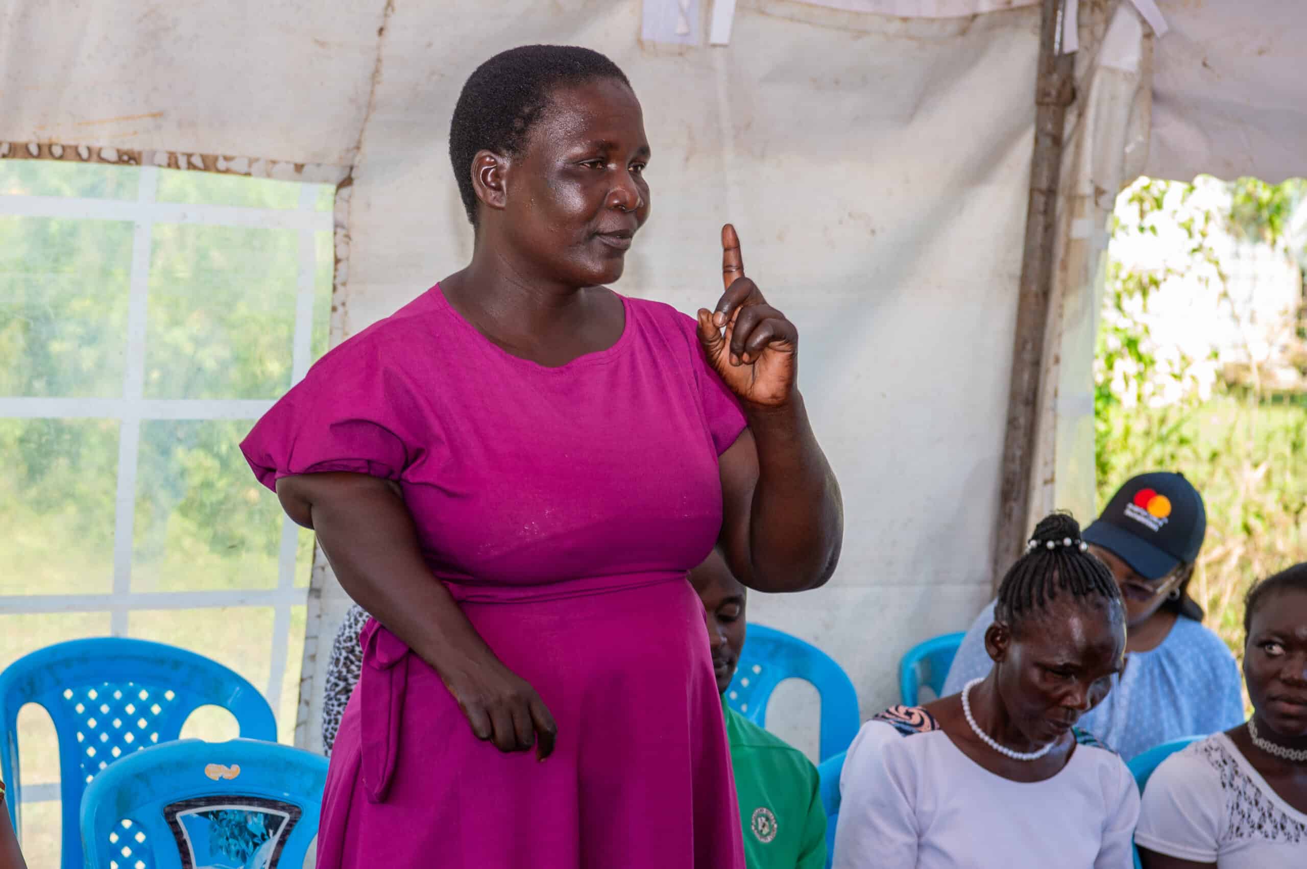 a woman in a vibrant pink dress is standing and addressing a group at an outdoor meeting